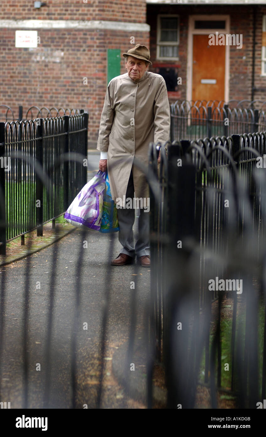 Uomo anziano che trasportano shopping e passeggiate home sul complesso residenziale nella zona est di Londra Foto Stock