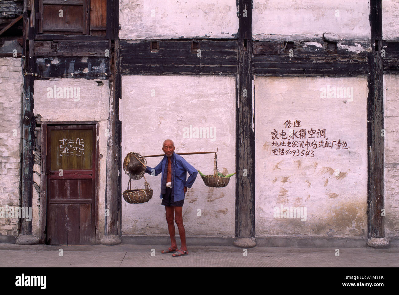 La Cina nella provincia di Zhejiang Shaoxing agricoltore spalla portante pole dal vecchio muro Foto Stock