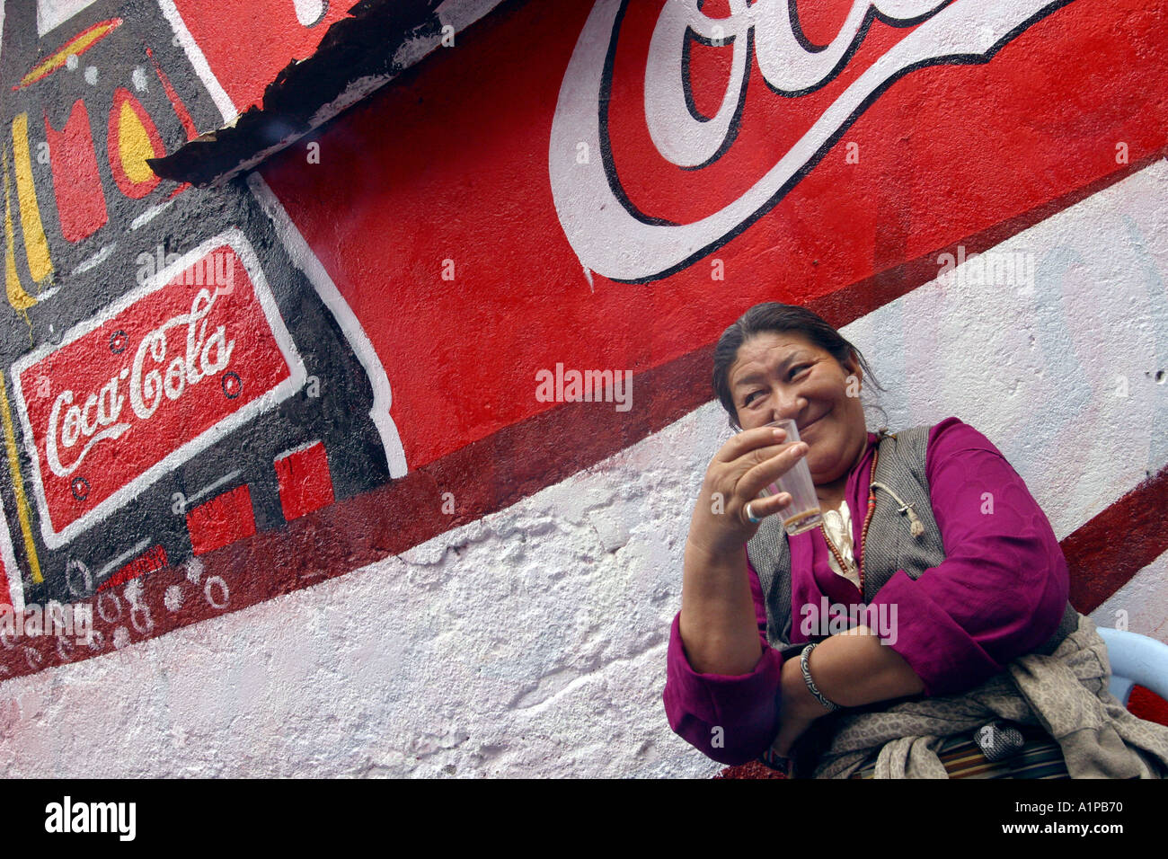 Una donna tibetana si siede di fronte a una grande coca cola pubblicità dipinta su un muro in Bodhgaya, in Bihar in India Foto Stock