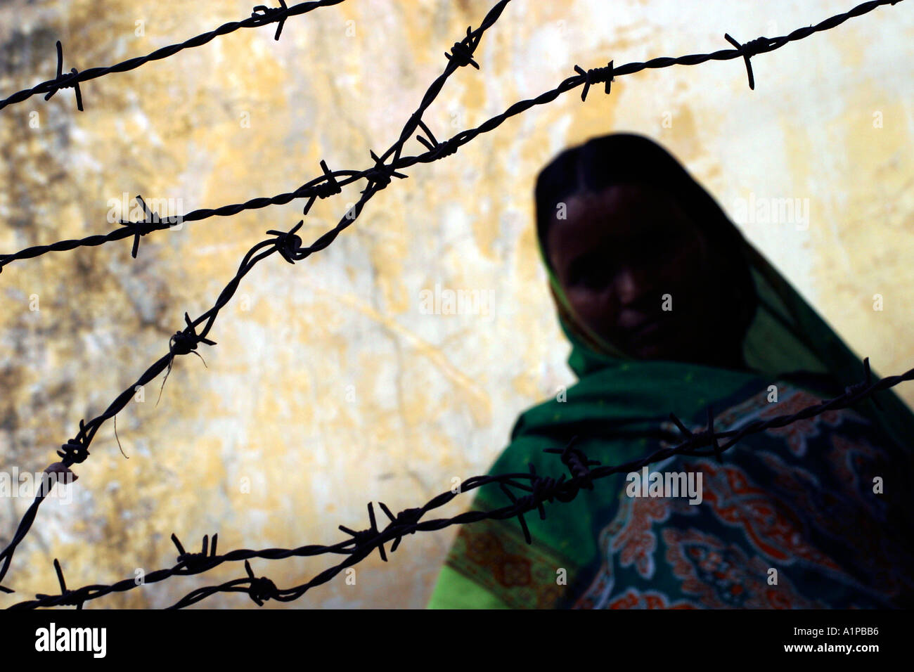 Una donna indiana si siede dietro una staccionata di filo spinato a Nuova Delhi in India Foto Stock