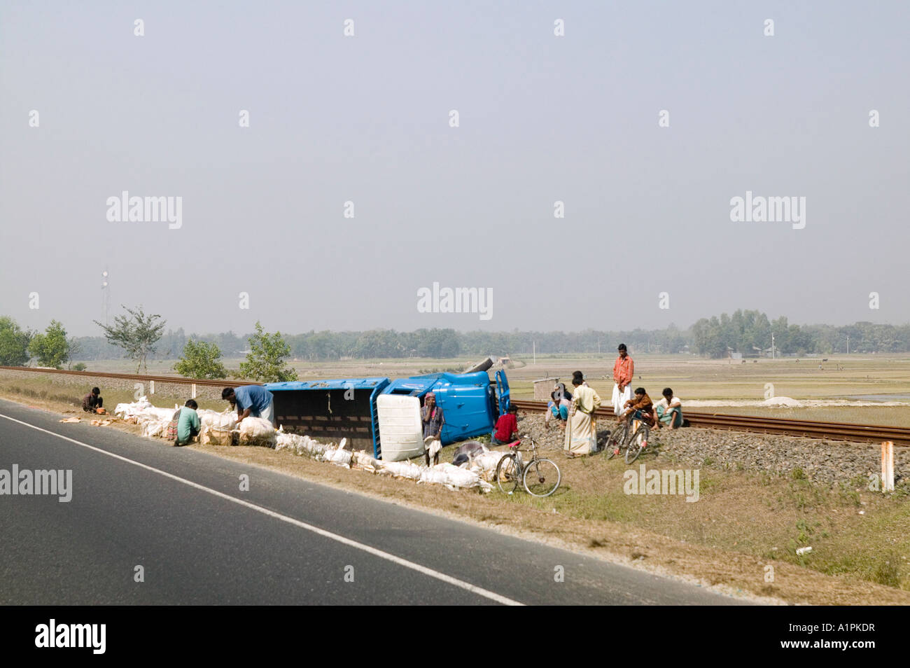 Attendere passeggeri lungo la strada con le merci dispersi dopo un camion ribaltato il Bangladesh Foto Stock