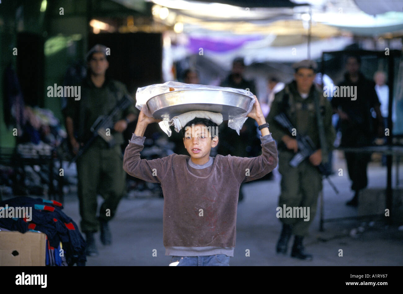 Coloni ebrei in Cisgiordania Hebron ragazzo palestinese vende la sua indossa nel mercato con la sua pattuglia di IDF IN BACKGROUND 1996 Foto Stock