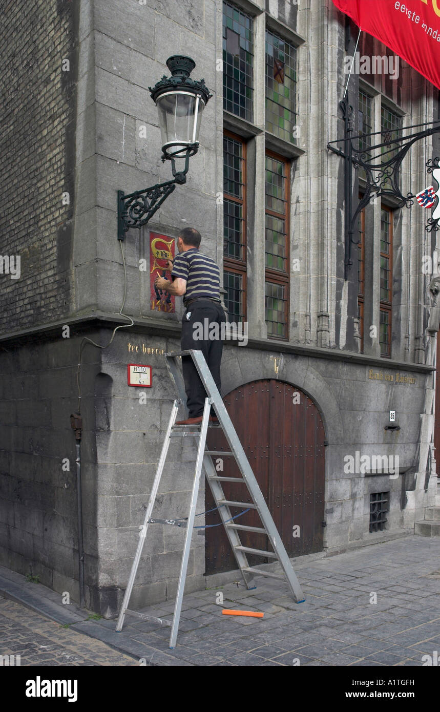 Un uomo su una scala di verniciatura di un segno su una parete in Bruges Belgio Foto Stock