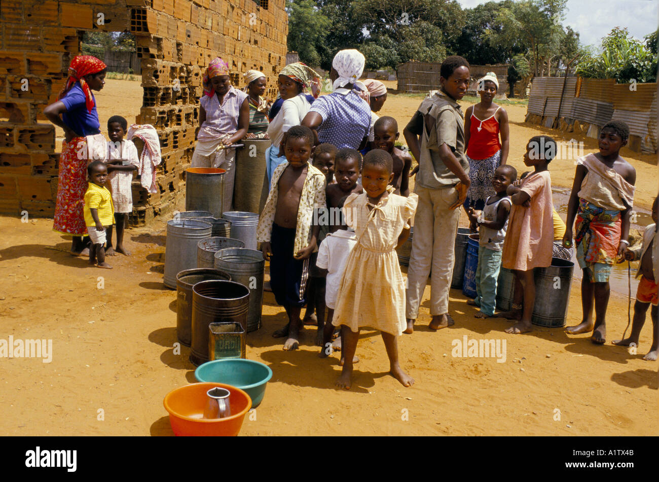 Donne e bambini SFOLLATI A CAUSA DELLA GUERRA messa in coda con benne a rubinetto di acqua STAND .MAPUTO BARRIO Foto Stock