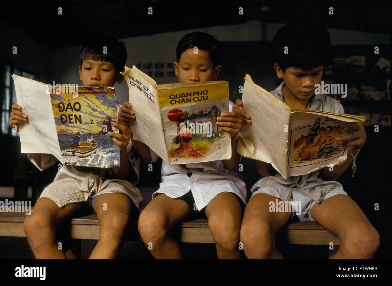 Tre bambini seduti su una panchina , leggere fumetti A SCUOLA IN VIETNAM Foto Stock