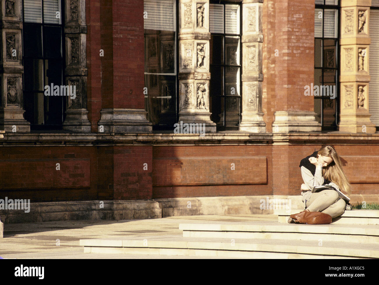 Lettura femminile seduti sui gradini fuori Victoria and Albert Museum di Londra Foto Stock