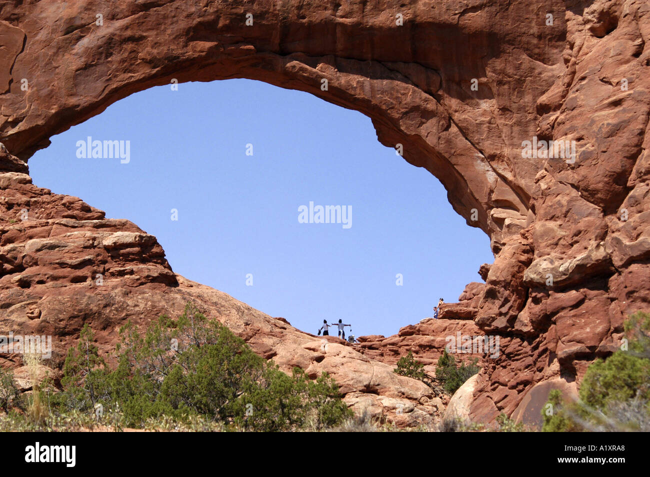 I turisti in posa per le fotografie sotto un enorme masso naturale arch Arches National Monument park. Moab Utah STATI UNITI D'AMERICA Foto Stock