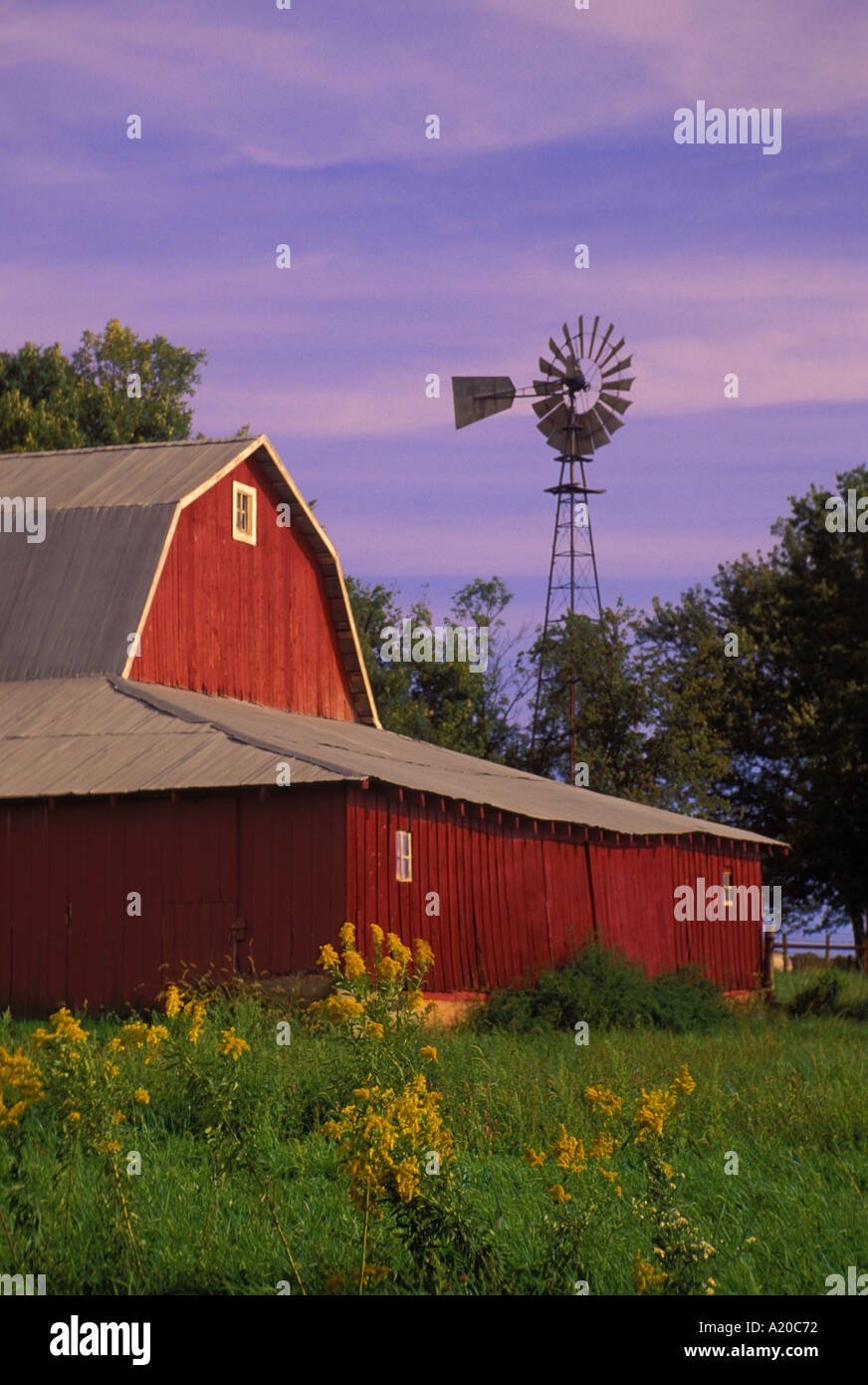 Nostalgia: un classico granaio rosso su una fattoria a gestione familiare con il vecchio mulino a vento evidenziata con un tramonto colorato come il crepuscolo si assesta, Missouri USA Foto Stock