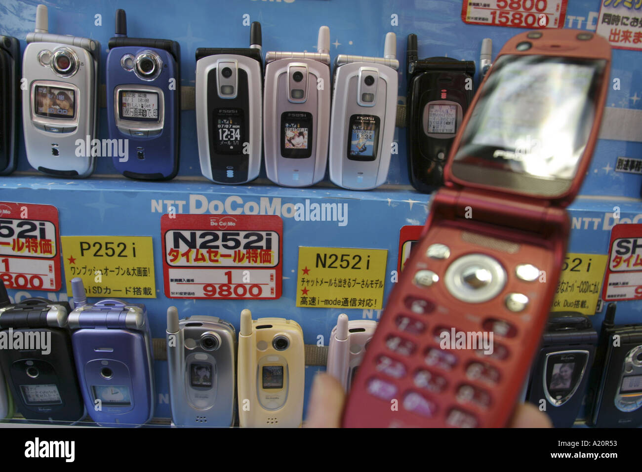 Mano che tiene in rosso di un telefono mobile in background righe di telefoni mobili da un NTT DoCoMo stand in un negozio di elettronica. Foto Stock