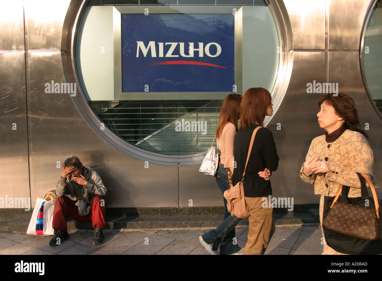 Un uomo senza tetto si trova al di fuori della banca Mizuho nel quartiere di Shinjuku a Tokyo, in Giappone. Foto Stock