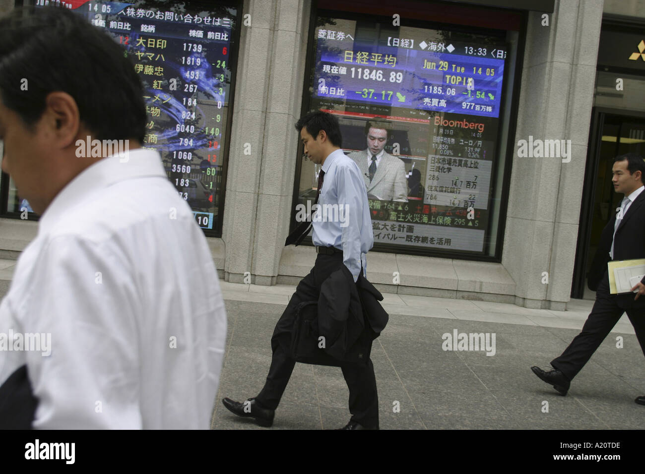 Le donne giapponesi a piedi passato una banca di scorte e condivide un monitor a schermo che mostra i valori più recenti di commodities, Tokyo, Giappone Foto Stock