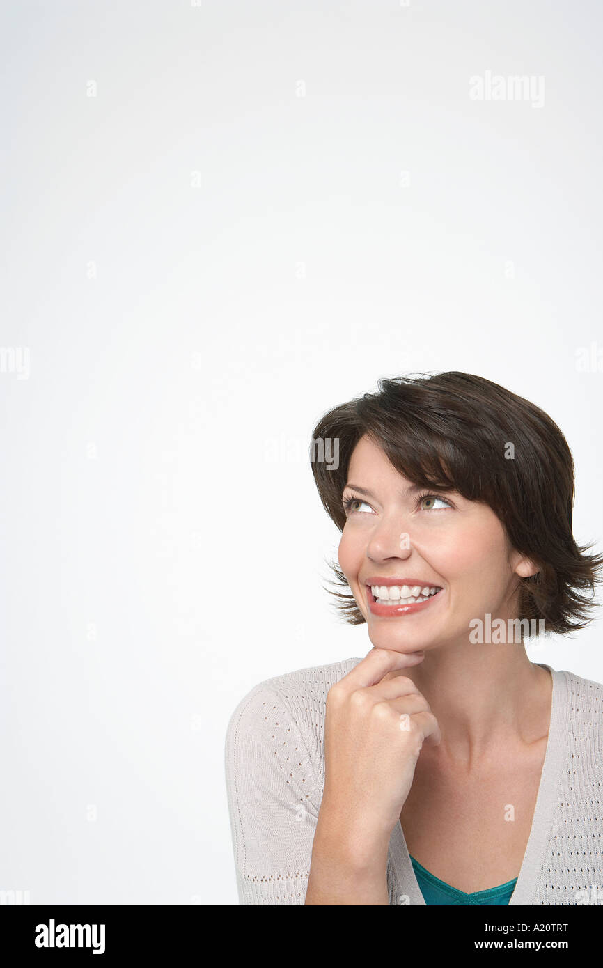 Donna sorridente guardando in alto, mano sul mento Foto Stock