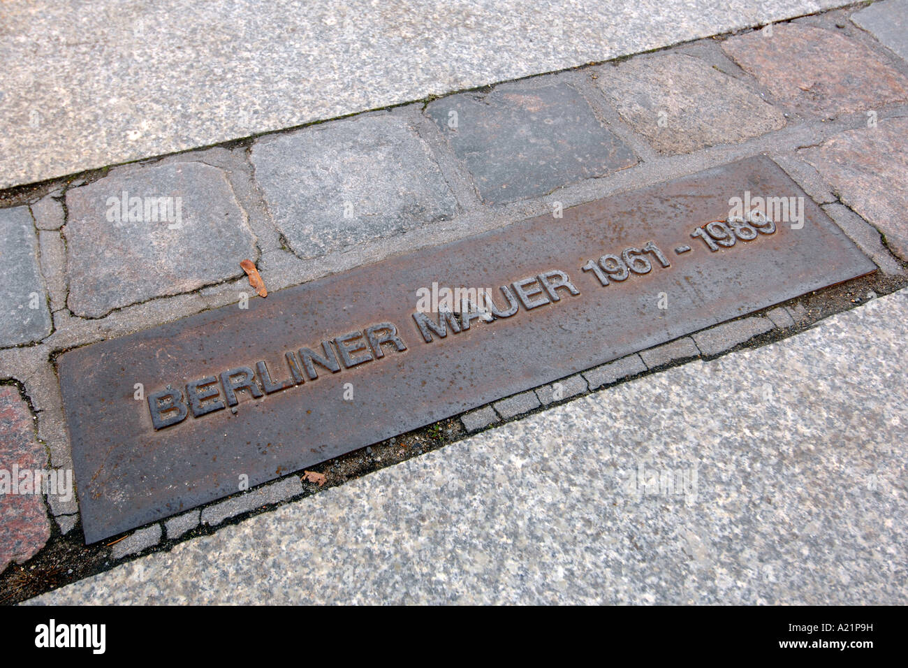 Una lapide commemorativa e linea doppia di pietre per pavimentazione che segna il percorso del Muro di Berlino in Germania. Foto Stock