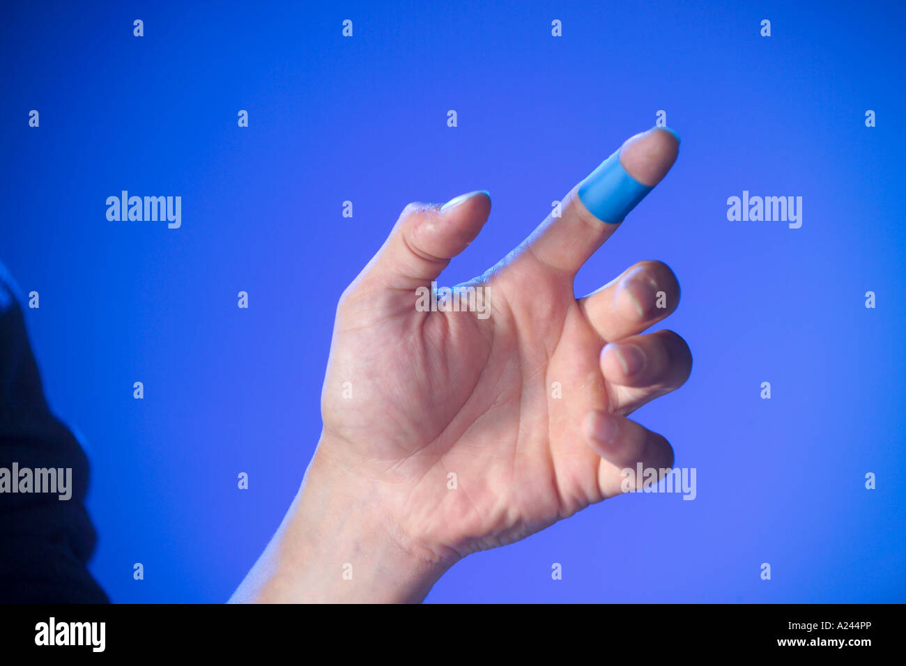 Ferito alla mano con blue ristorazione gesso dito su sfondo blu Foto Stock