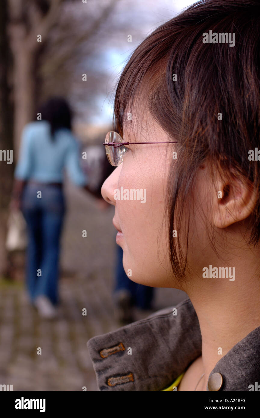 Ritratto di attraente giovane donna asiatica vista laterale altre persone al di fuori della messa a fuoco in background Foto Stock