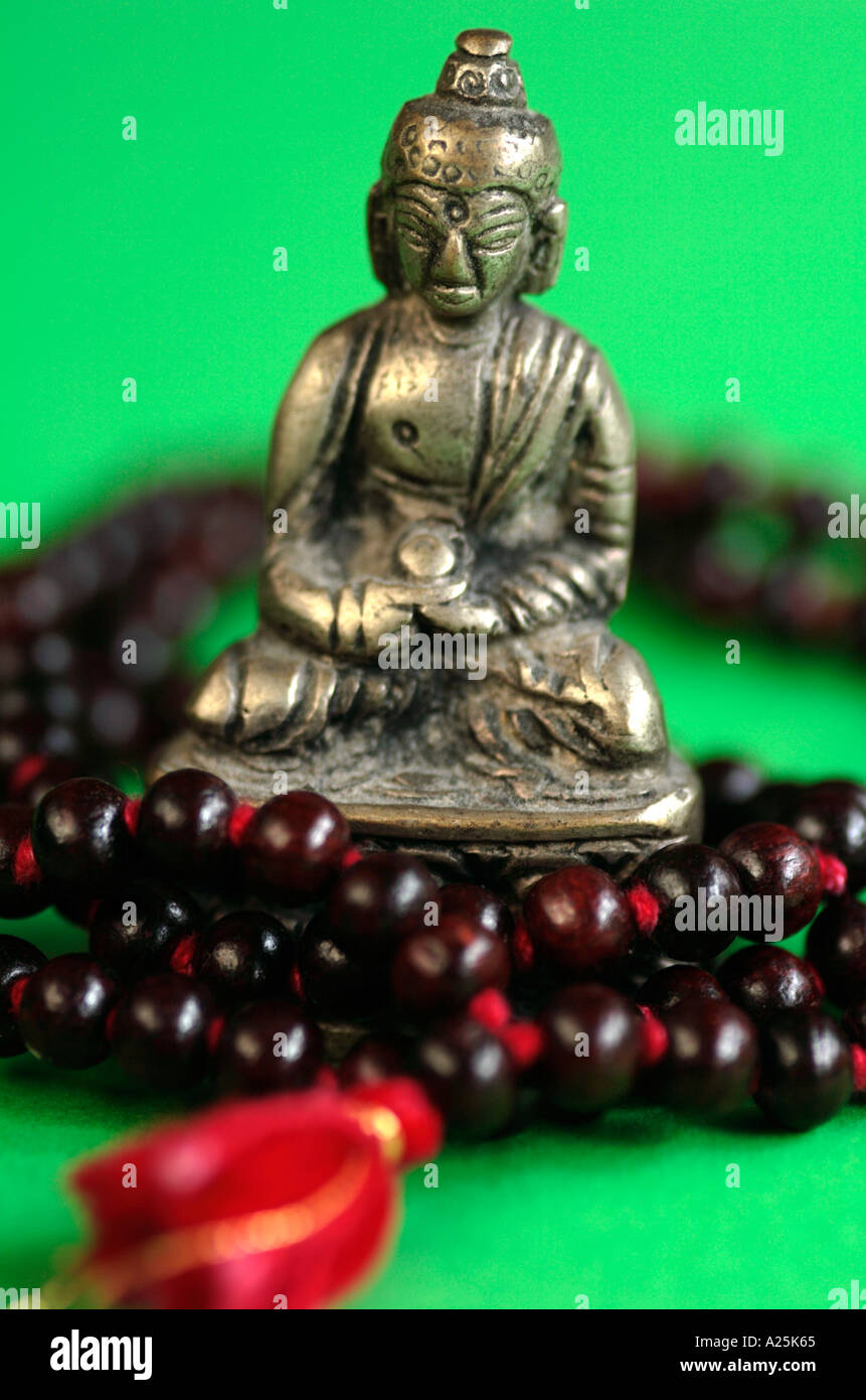 Chiusura del Buddha in ottone con perle di rosso e nastro contro lo sfondo di colore verde Foto Stock