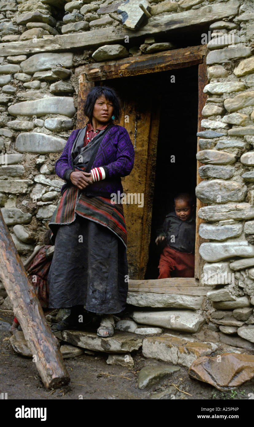Il nepalese la madre e il bambino a stare di fronte ad un tradizionale fango e casa di pietra in alto a fare TARAP VALLEY DOLPO NEPAL Foto Stock