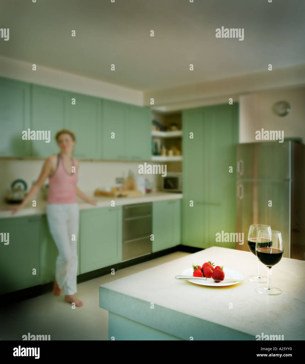 Tall donna bionda nella sua cucina, shot incentrata sul primo piano con vino rosso e fragole Foto Stock