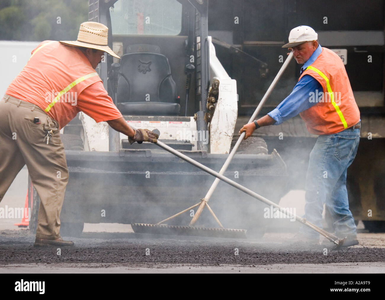 Due uomini con rastrelli, levigatura asfalto caldo come lavorano su strada in costruzione. Foto Stock