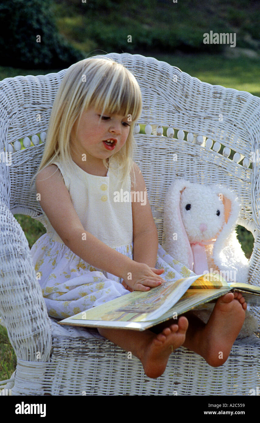 Adorabile bambina seduti su una sedia di vimini e la lettura di un peluche Foto Stock