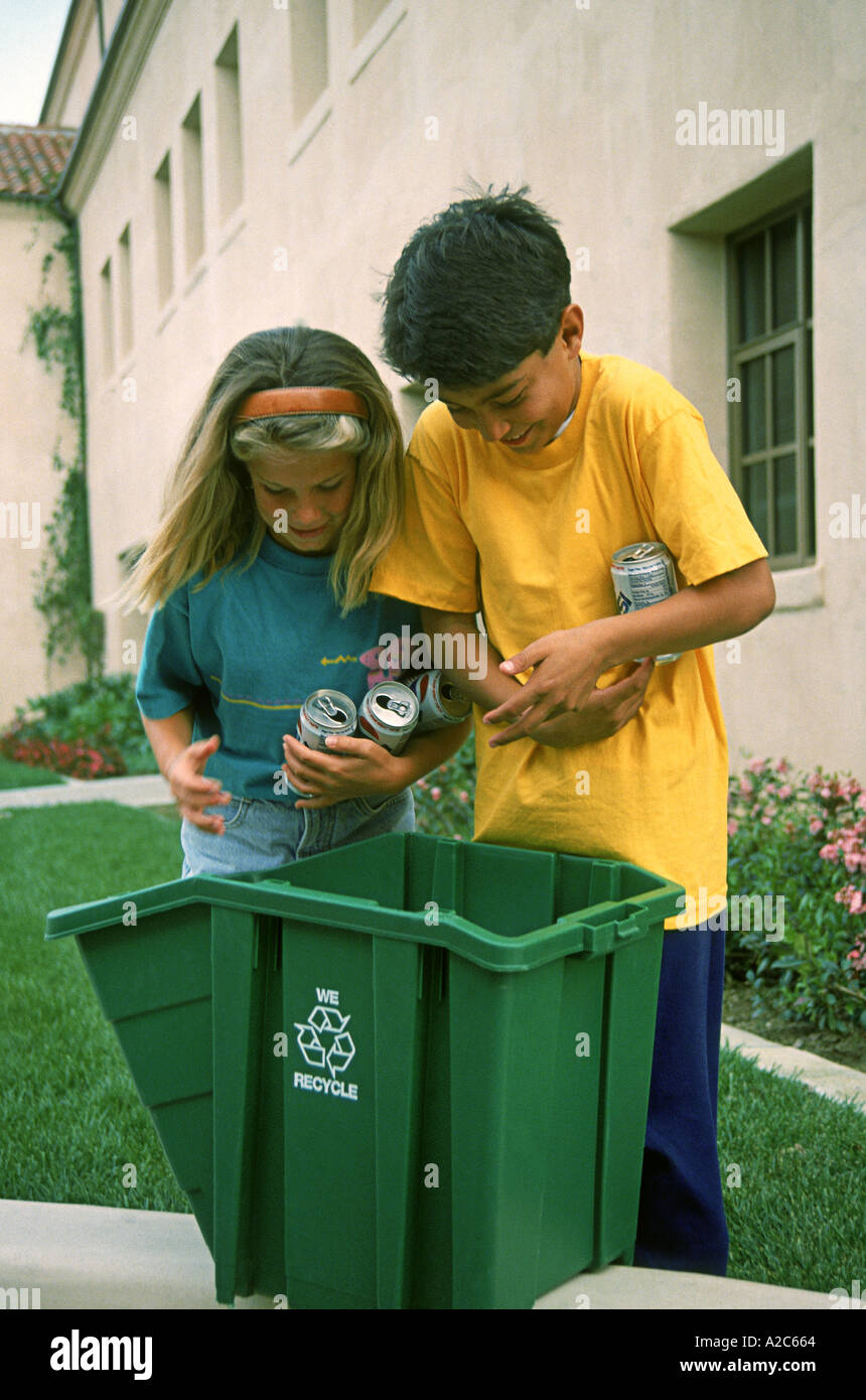 Due bambini da 7 anno a 8 anni mettendo le lattine in un contenitore di riciclaggio per la raccolta POV SIGNOR © Myrleen Pearson Foto Stock