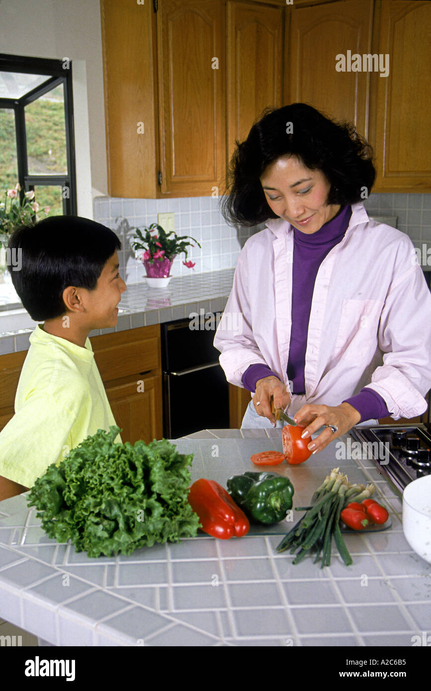 Americano cinese di ascolto madre suo figlio lavora in cucina di preparare la cena insalata di diversità etniche diverse multiculturale razziale multi pov stare insieme Foto Stock
