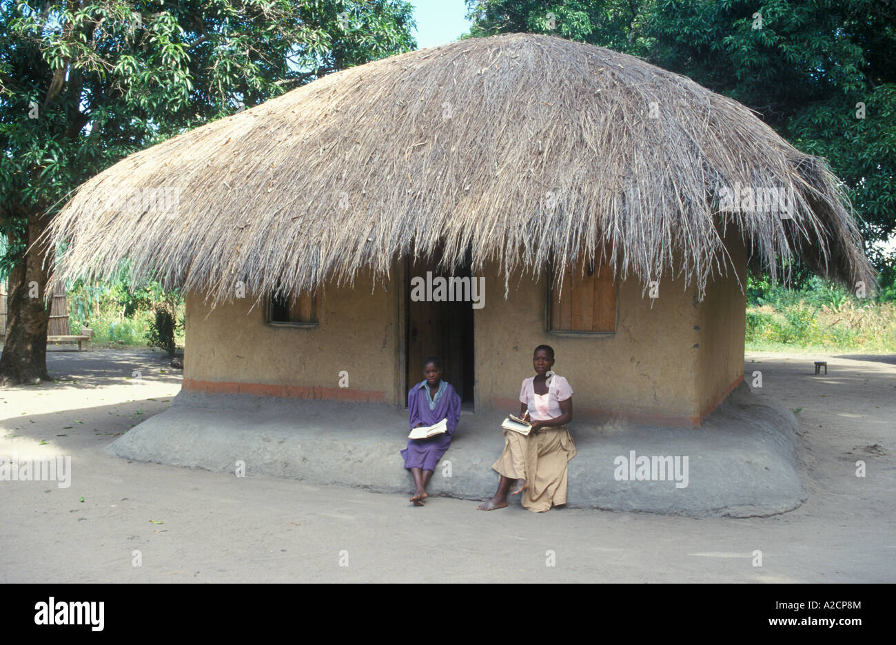 Due giovani donne seduti di fronte a una cannuccia di capanna con il tetto di paglia in un villaggio vicino a Spiaggia di Kande presso il Lago Malawi in Africa Foto Stock