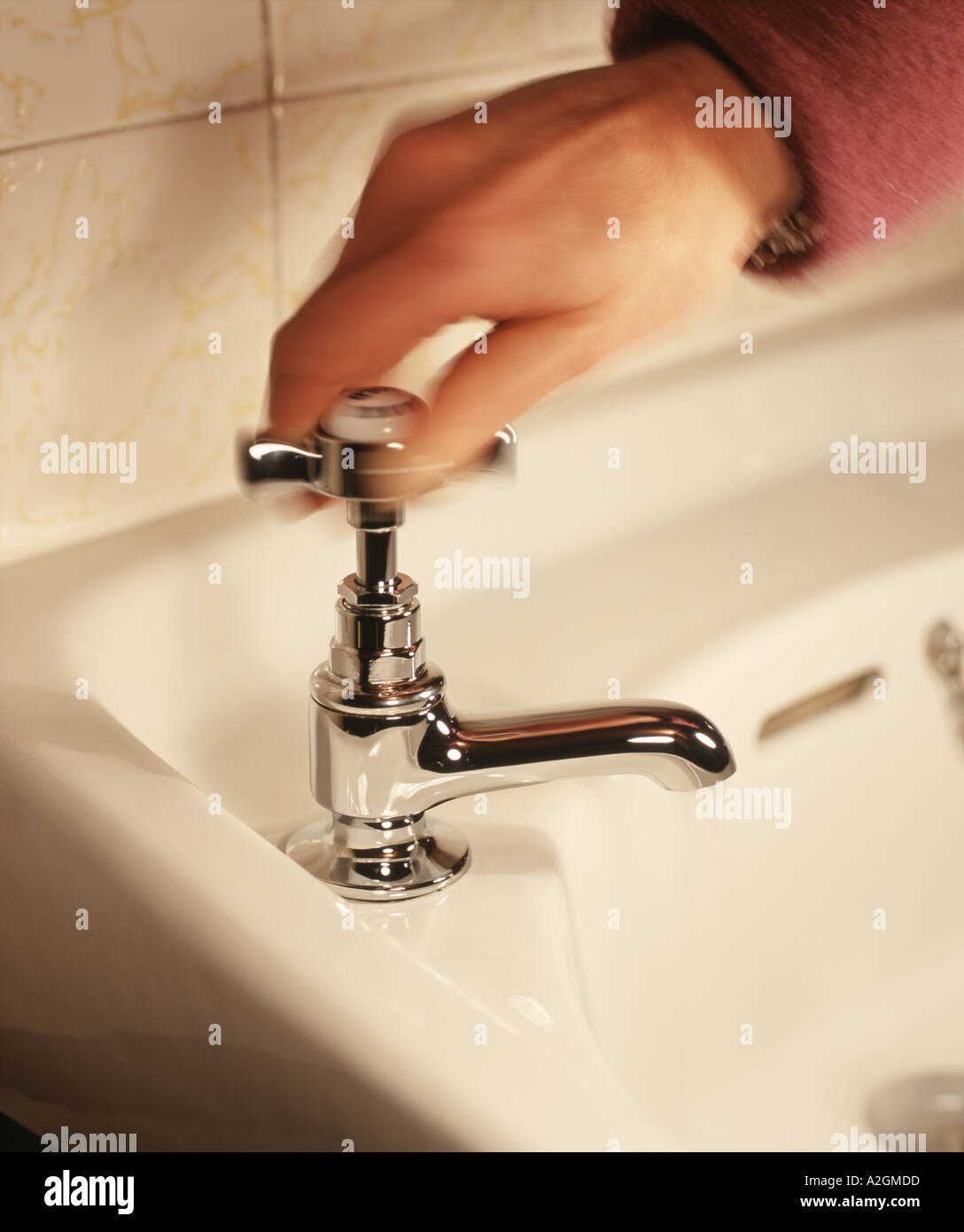 Una mano di donna si spegne l'acqua che scorre da un bagno di cromo tocca Foto Stock