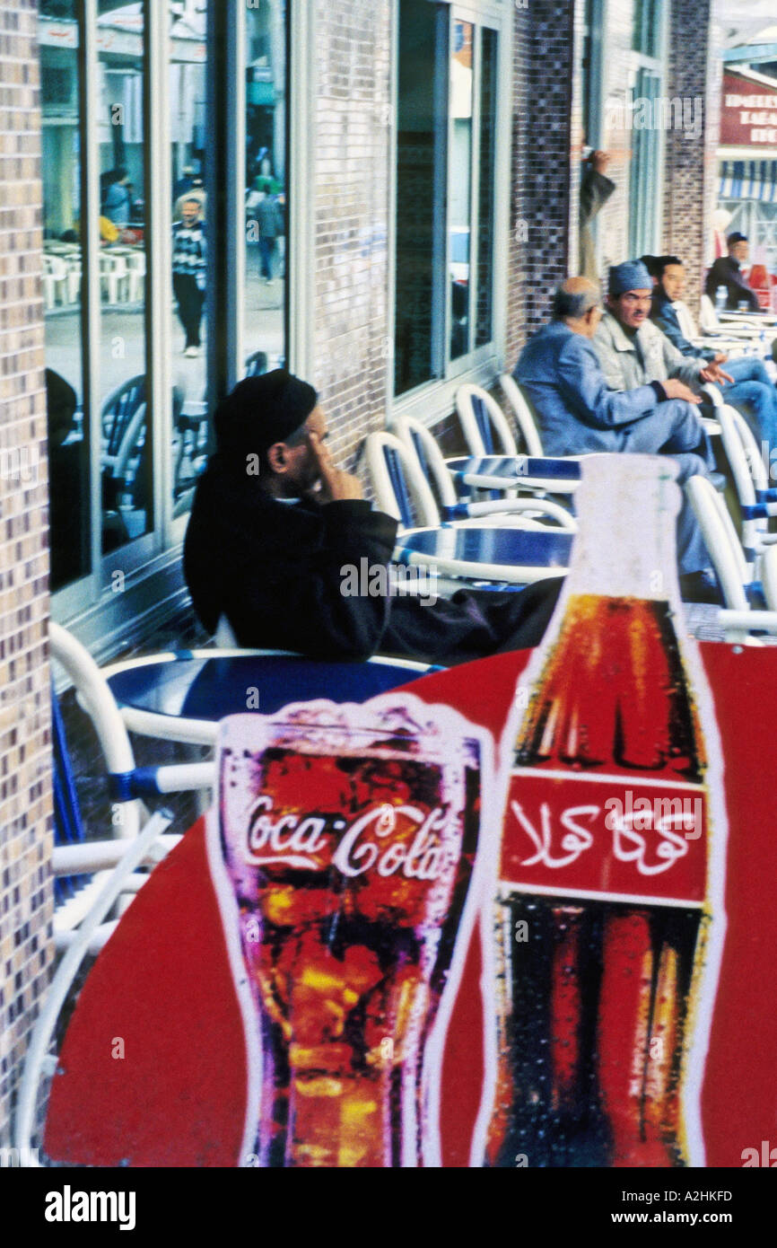 AFRICA MAROCCO Tangeri uomini marocchini seduti ad un cafe' all'aperto che visualizza un messaggio pubblicitario per la Coca Cola in arabo Foto Stock