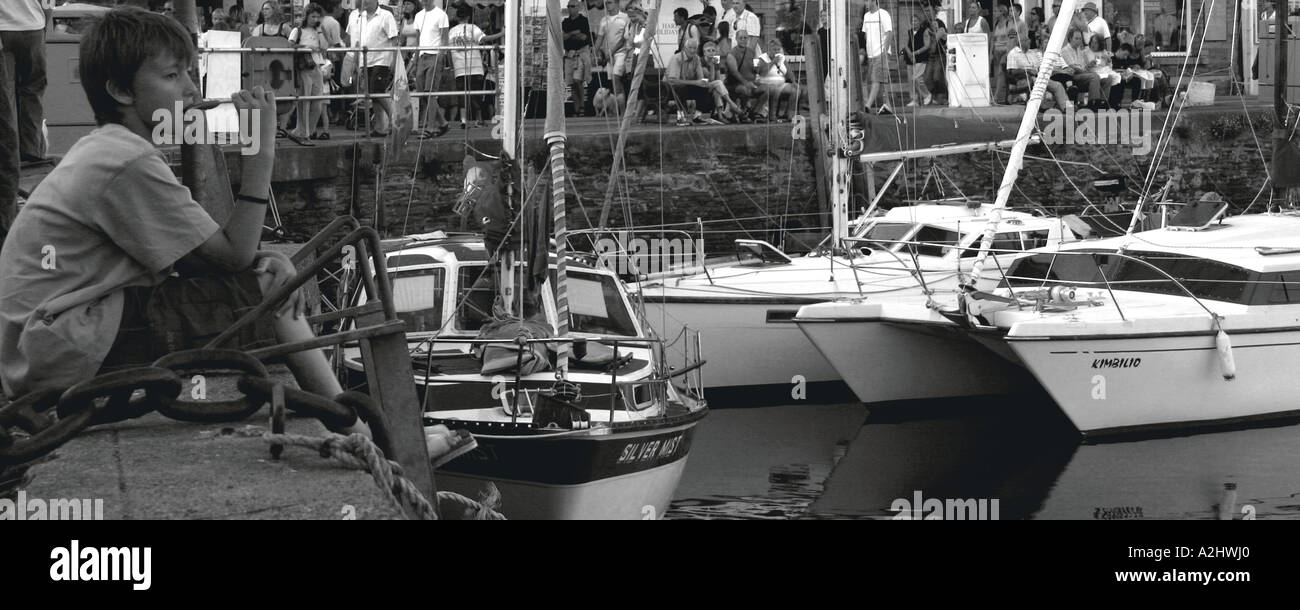 Foto in bianco e nero di un ragazzo di mangiare un gelato seduto sulla banchina della baia a Padstow, Cornwall, Inghilterra Foto Stock