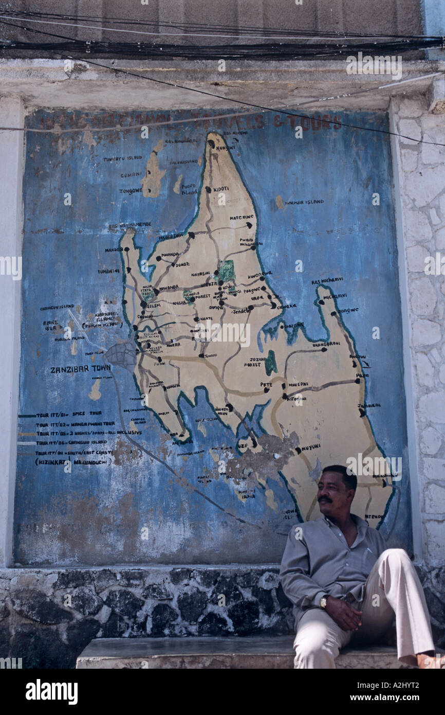 In Stone Town, la piccola capitale di Zanzibar, un uomo si rilassa sotto una mappa di Zanzibar dipinta su una parete Foto Stock