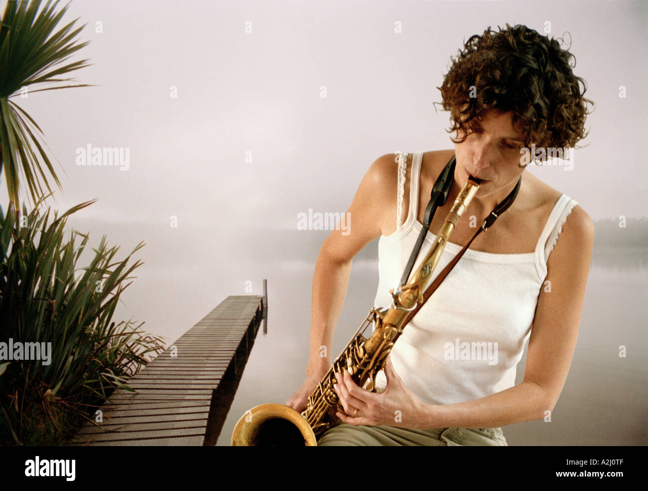 Donna suonare il sassofono da un lago. Foto Stock