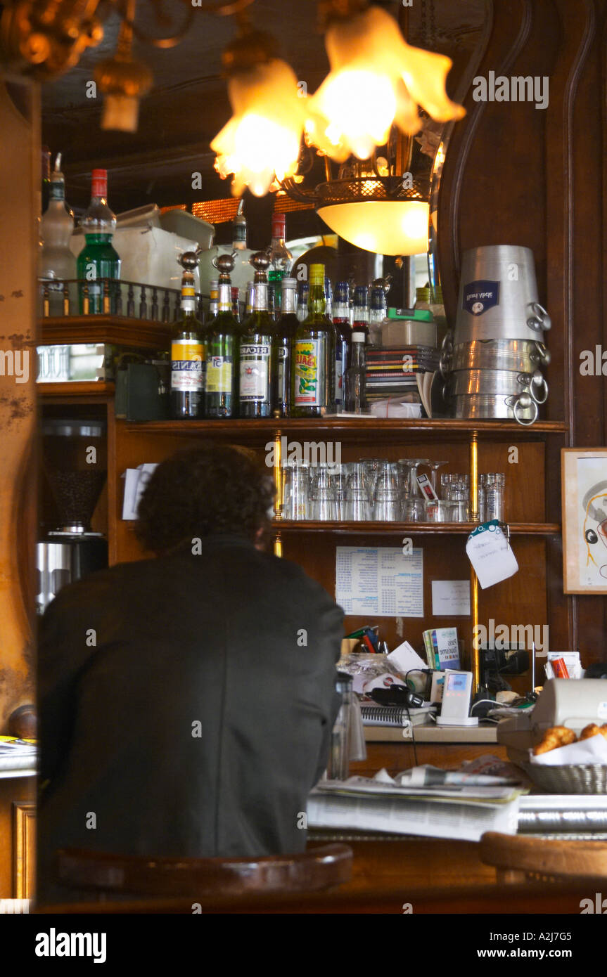 Un Uomo in camicia nera seduti al bar la lettura di una carta da giornale e  bere. Mensole con bottiglie e bicchieri e secchielli per il ghiaccio. Il  Bistrot du peintre è