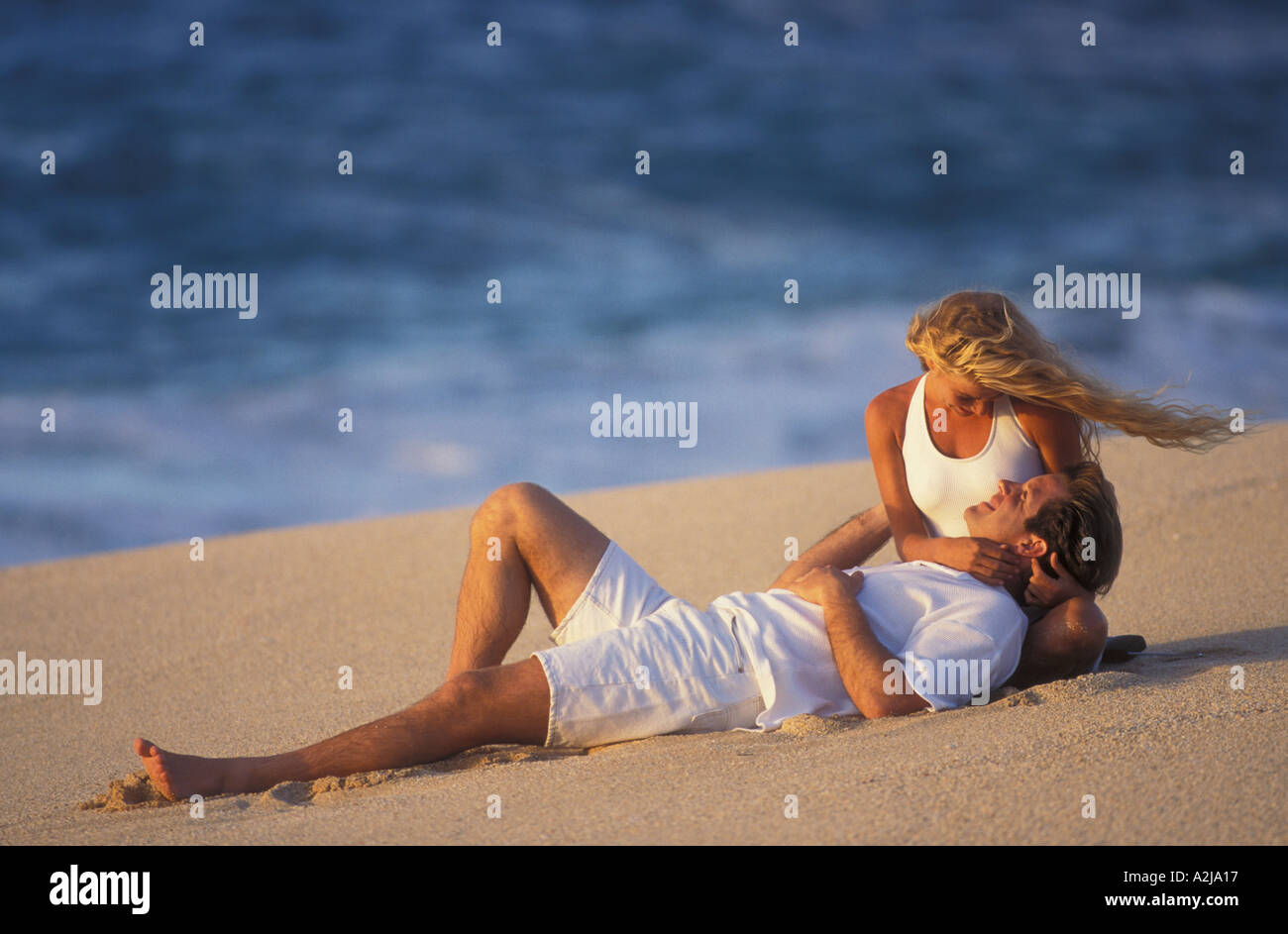 L'uomo guarda in faccia di una seduta donna bionda come egli si appoggia la sua testa nel suo giro mentre giacenti su di una spiaggia di sabbia Foto Stock