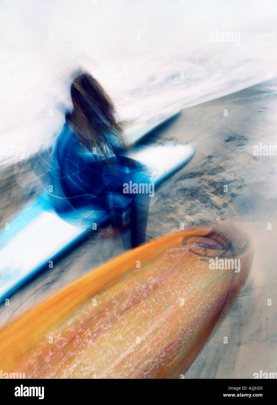 Surfista femmina seduto sulla spiaggia sulla sua tavola da surf. L'immagine viene formato verticale e le caratteristiche di movimento. Foto Stock