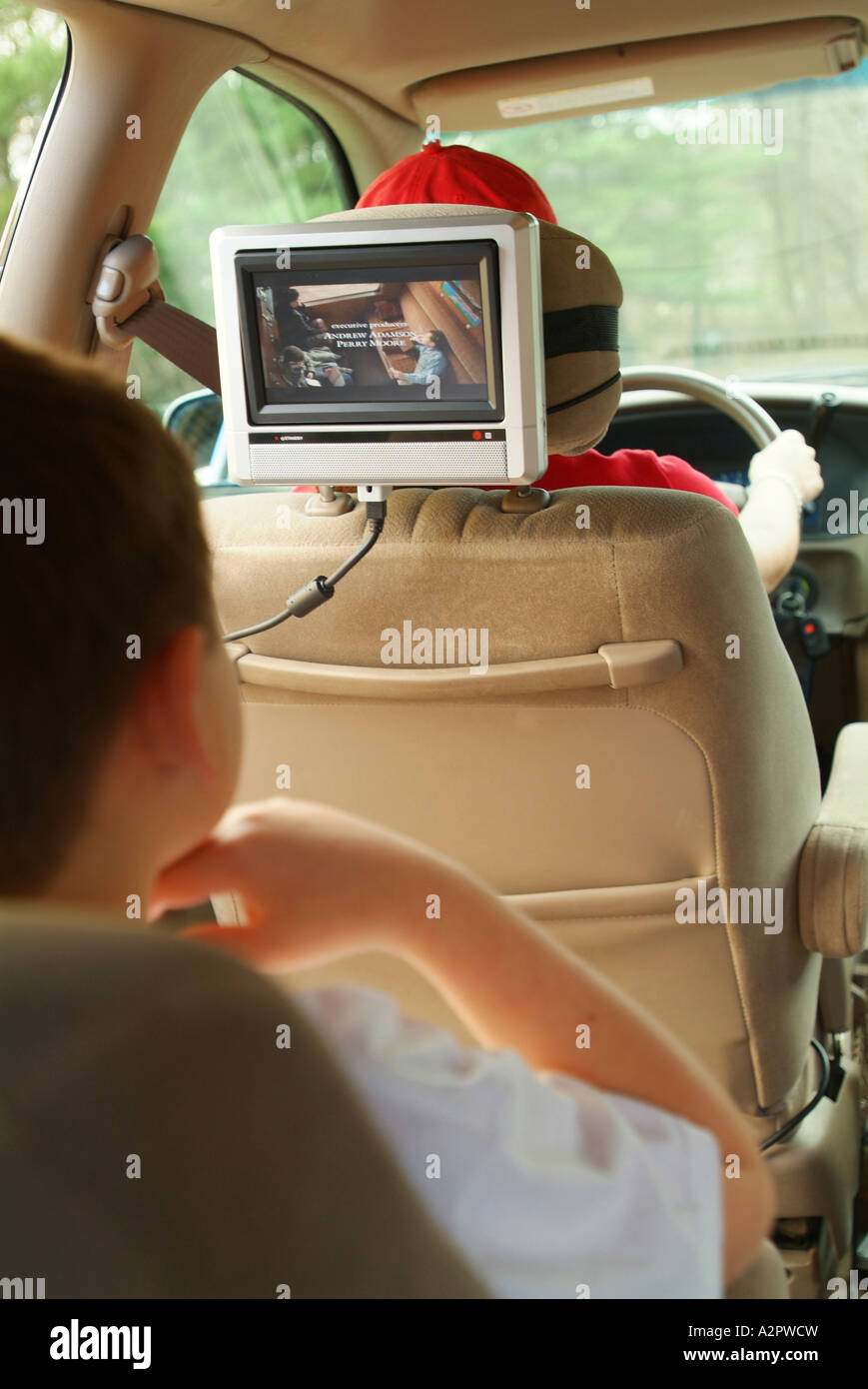 Un bambino di 8 anni ragazzo bianco guarda un film su un DVD player in un mini van automobile mentre la sua mamma aziona la macchina Foto Stock