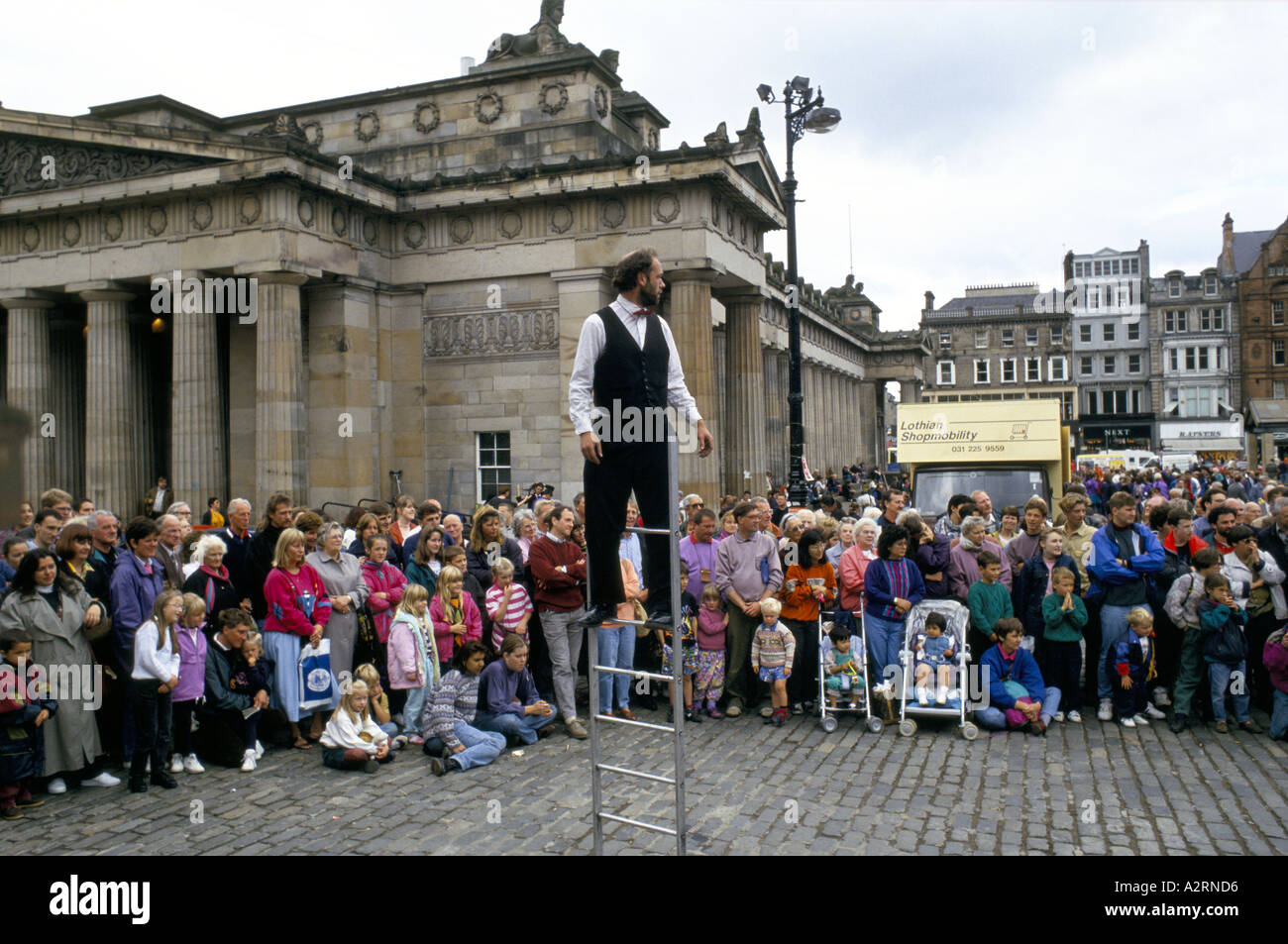 Un esecutore di strada in piedi sulla scaletta orologi folla Edinburgh Fringe Festival Foto Stock