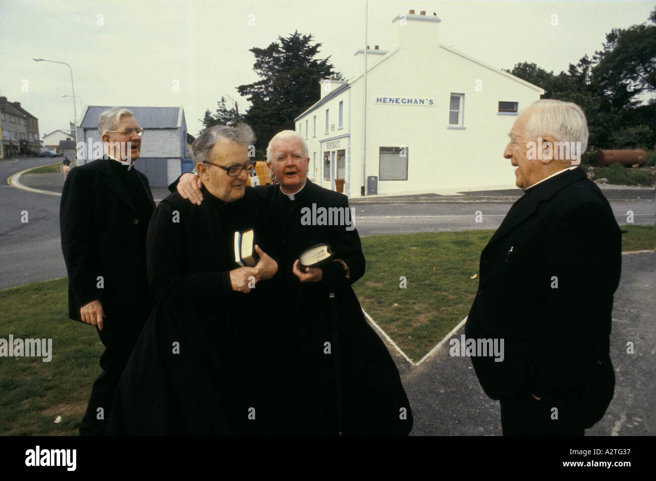 Quattro sacerdoti holding bibbie ridere abbracciando in piedi sul angolo di strada eire Foto Stock