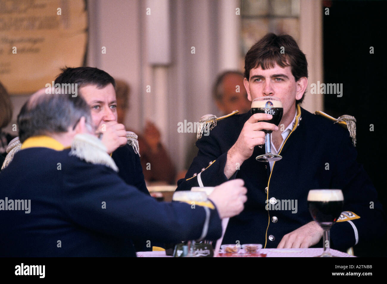 Uomini vestiti in uniforme di bere birra leffe al di fuori di un cafe Anversa in Belgio Foto Stock