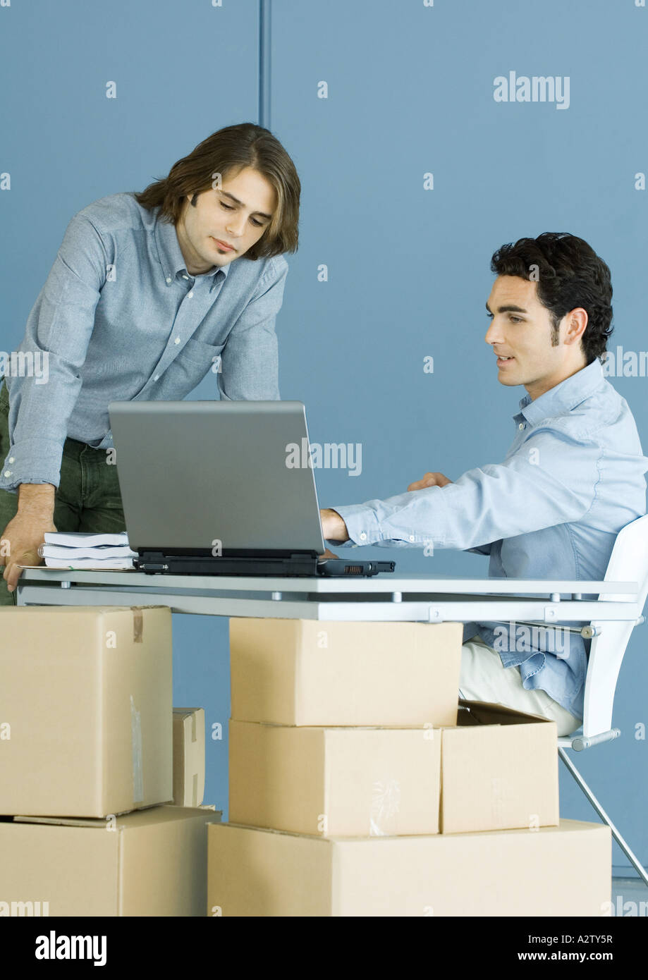 Due colleghi di sesso maschile a parlare attraverso escursioni, scatole di cartone in primo piano Foto Stock