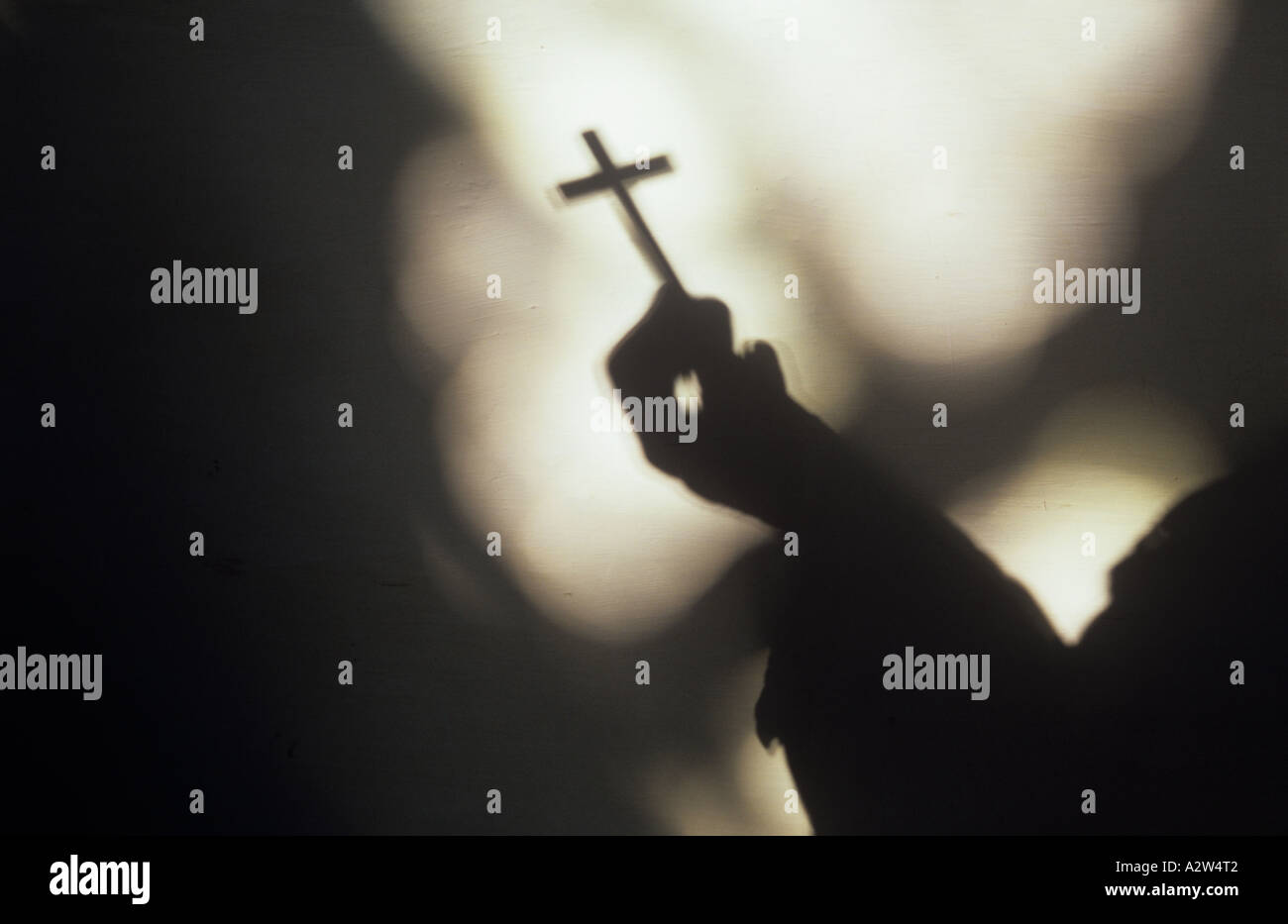 Ombra di monklike figura tenendo piccolo crocefisso con altre ombre sulla parete pallido di ornati in chiaro Vetrate di chiesa Foto Stock