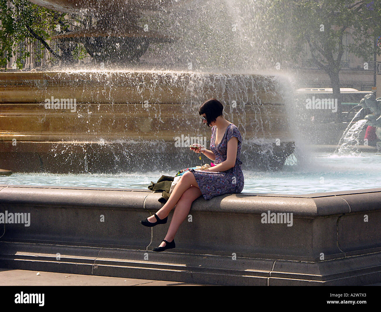 Un giovane turista femminile la scrittura di un messaggio di testo sul suo telefono cellulare in corrispondenza di una fontana a Londra nel maggio Foto Stock