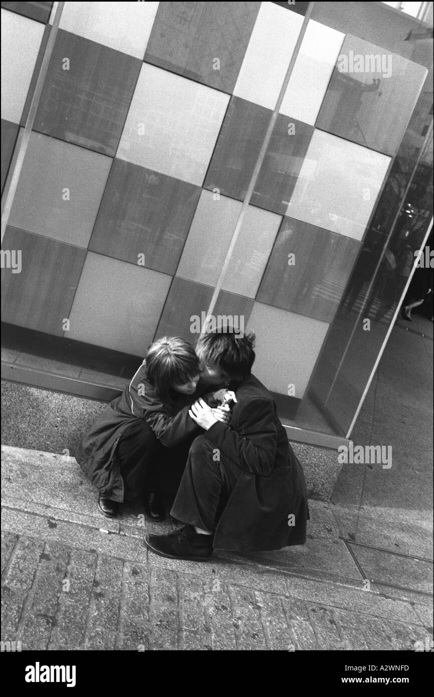 Giovane coppia corteggiamento kissing come essi squat sul terreno al di fuori di Starbucks nel quartiere Shibuya Foto Stock