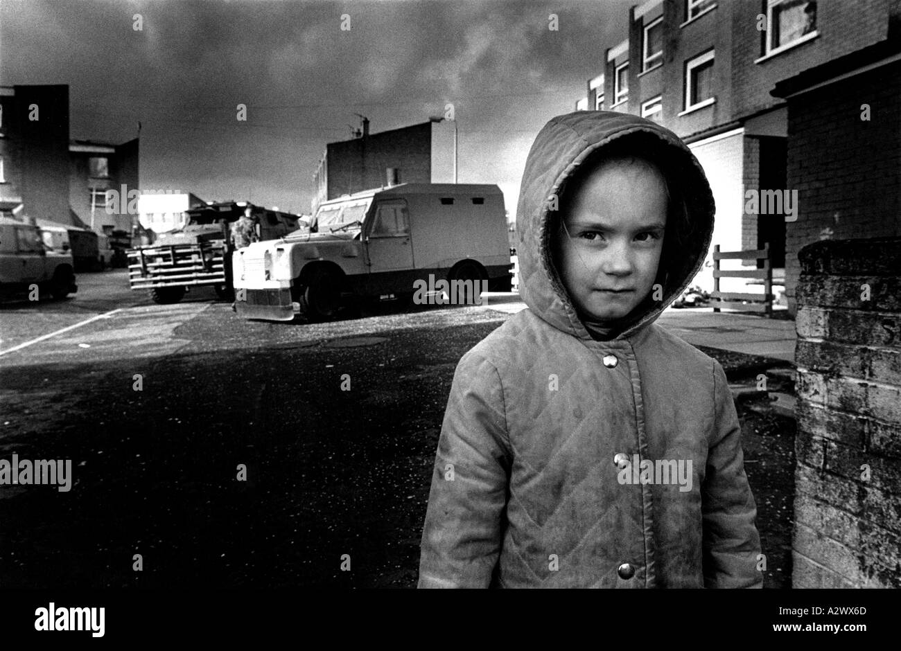 Un bambino sta in strada mentre una casa ricerca viene eseguita in background, Ballymurphy, Belfast, Irlanda del Nord Foto Stock