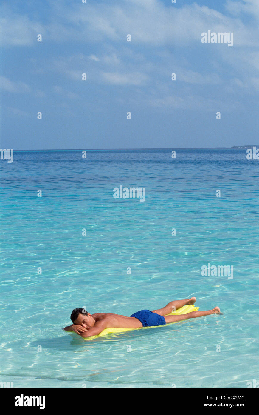 Maldive. Giovane uomo in costume da bagno sul letto aria galleggianti su acqua cristallina. Foto Stock