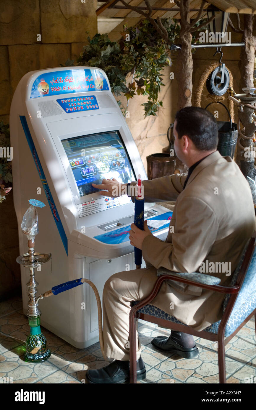 Un arabo Gentiluomo gioca a un videogame hotel macchina e gode di una tubazione Shisha. Dubai, Emirati arabi uniti Foto Stock