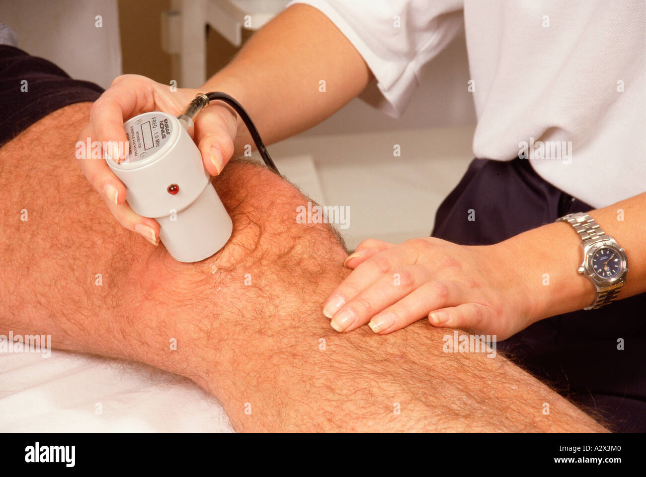 Ospedale Reparto di fisioterapia. Close-up mani del fisioterapista utilizzando apparecchiature a ultrasuoni per trattare il paziente di sesso maschile del ginocchio. Foto Stock
