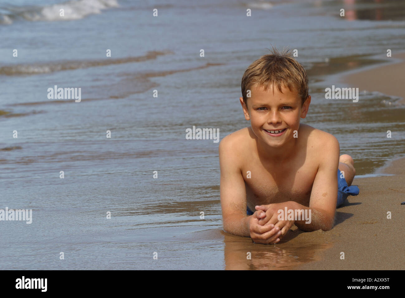 Giovane ragazzo caucasico bianco invecchiato di dieci anni che giace sulla spiaggia di sabbia di costa del mare Foto Stock