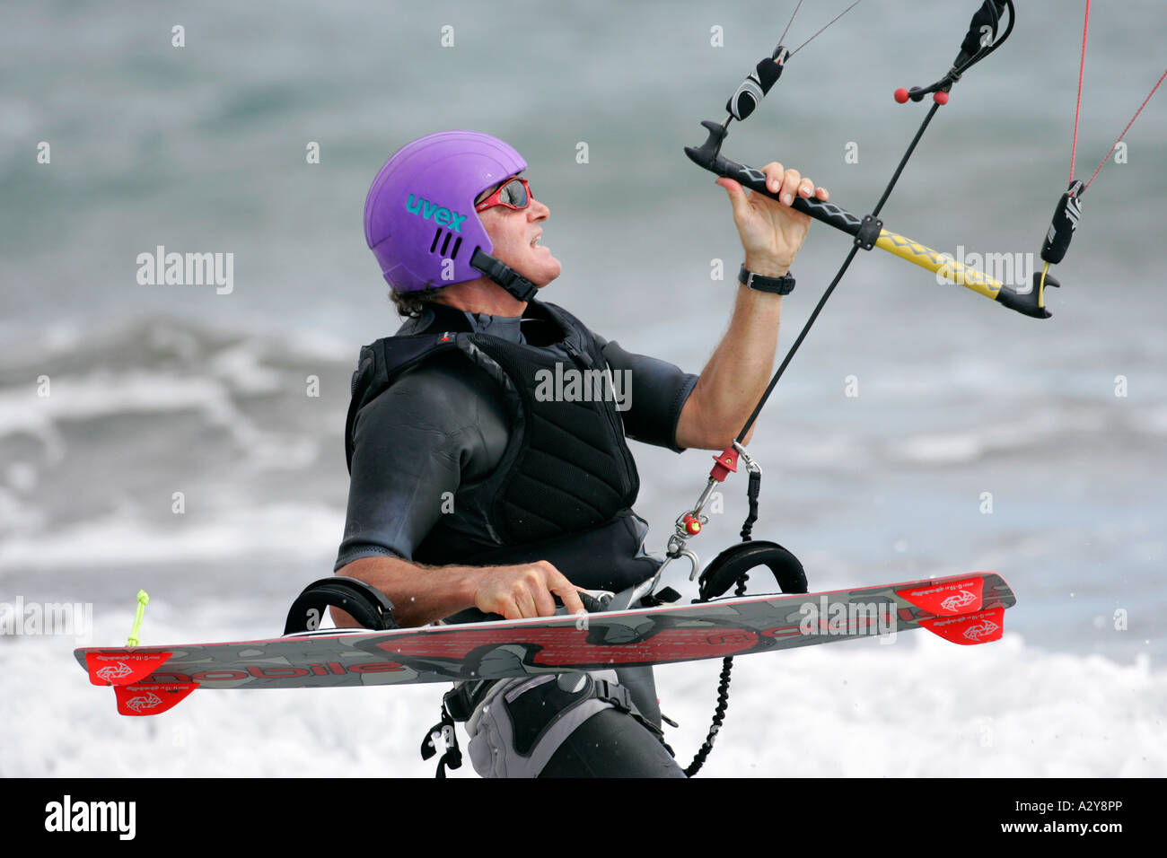 Kitesurfer maschio in muta nero e viola casco porta il suo bordo e controlla il suo kite Foto Stock