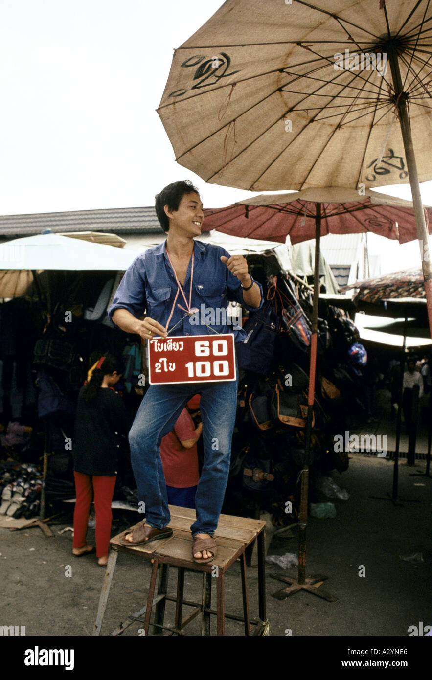 Uomo in piedi su uno sgabello con segno di prezzo intorno al suo collo pubblicità occasioni presso il mercato del fine settimana di Chatuchak a Bangkok Foto Stock
